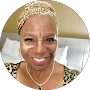 Smiling woman wearing a patterned headband, leopard print top, and necklace sits in front of a pillow and beige wall, ready to share her glowing testimonials.