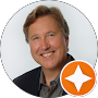 Portrait of a smiling man with light brown hair, wearing a suit jacket and shirt, featuring an orange and white star icon in the lower right corner to highlight testimonials.