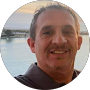 A man smiles at the camera with a body of water and a sunset in the background, capturing a perfect moment for heartfelt testimonials.